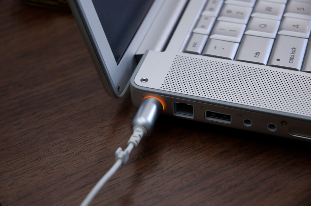 Laptop plugged in and charging. Shallow DOF, focus on orange light.